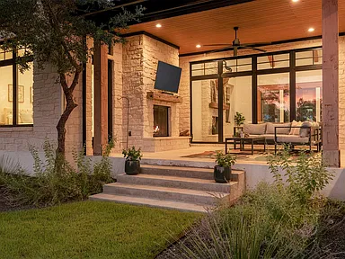 Covered outdoor living area with integrated television and architectural lighting at dusk