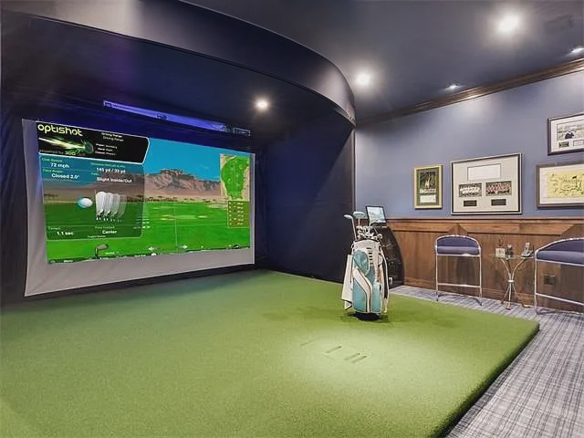 Golf simulator room with a large impact screen, putting turf, and club storage beside paneled walls