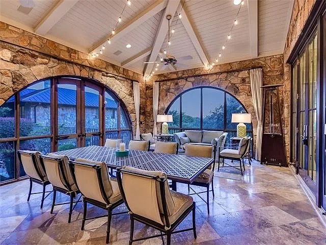 Covered stone patio with arched windows, string lighting, and dining under a vaulted ceiling