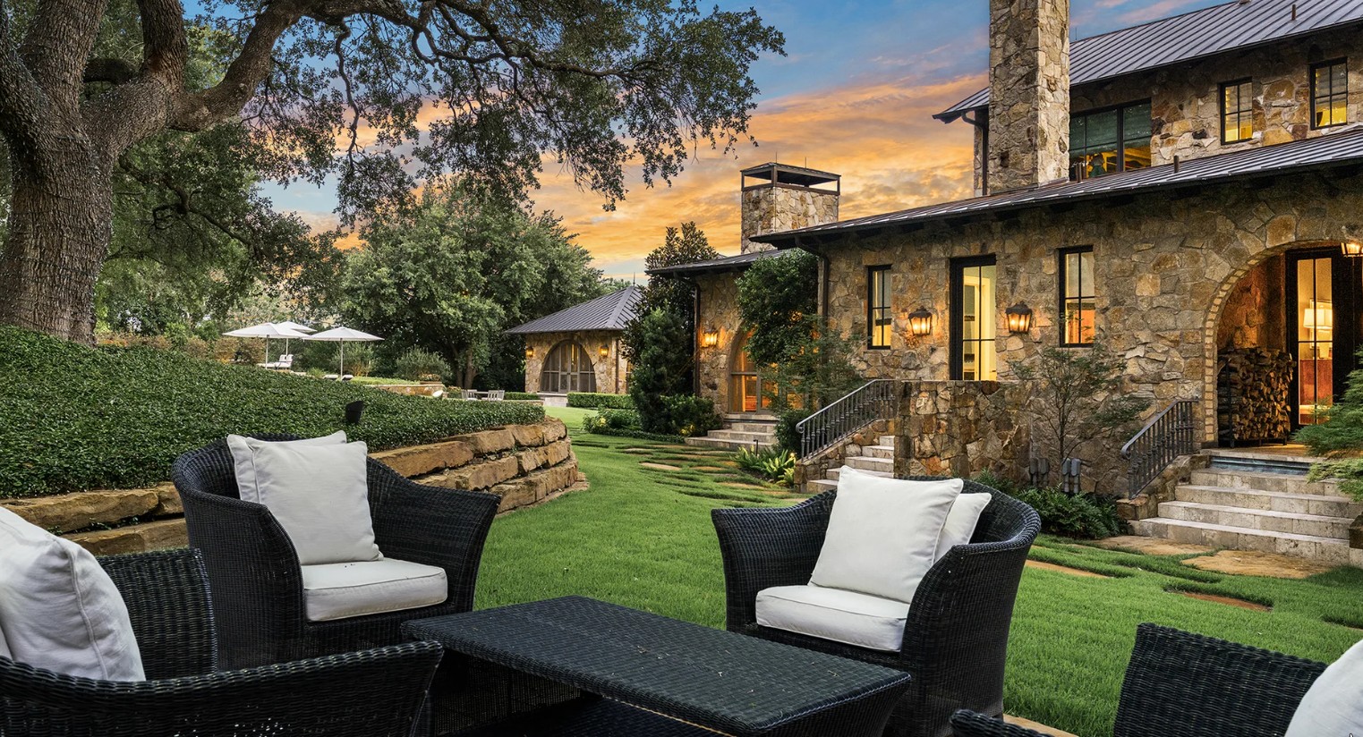 Stone terrace at dusk with outdoor seating, landscape lighting, and the residence beyond