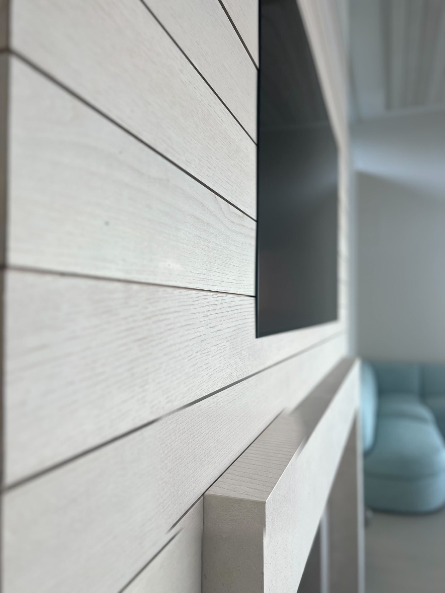 Close view of a flush-mounted television against white oak paneling above the mantel