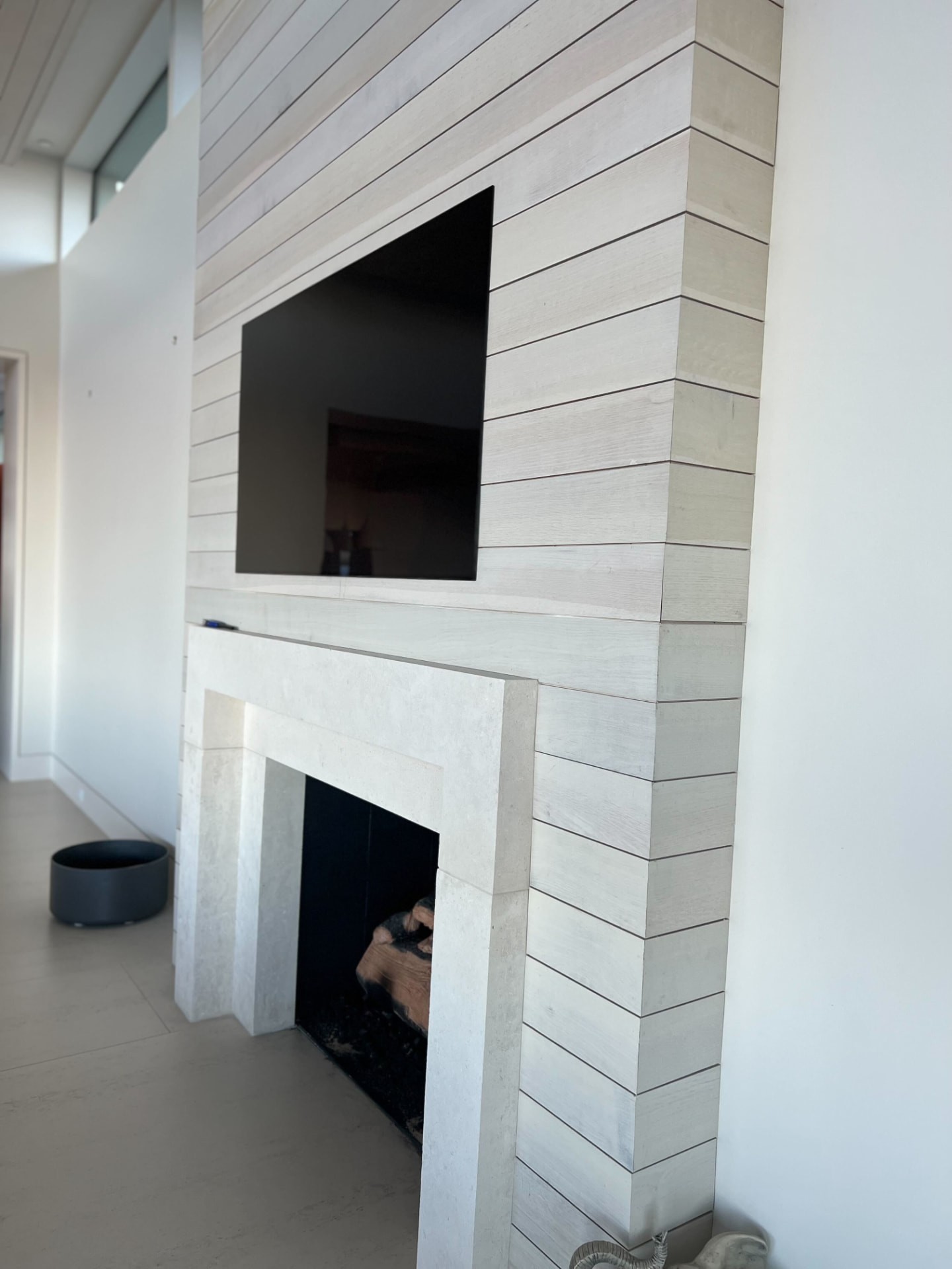 Television mounted above a limestone fireplace on a white oak slat chimney breast