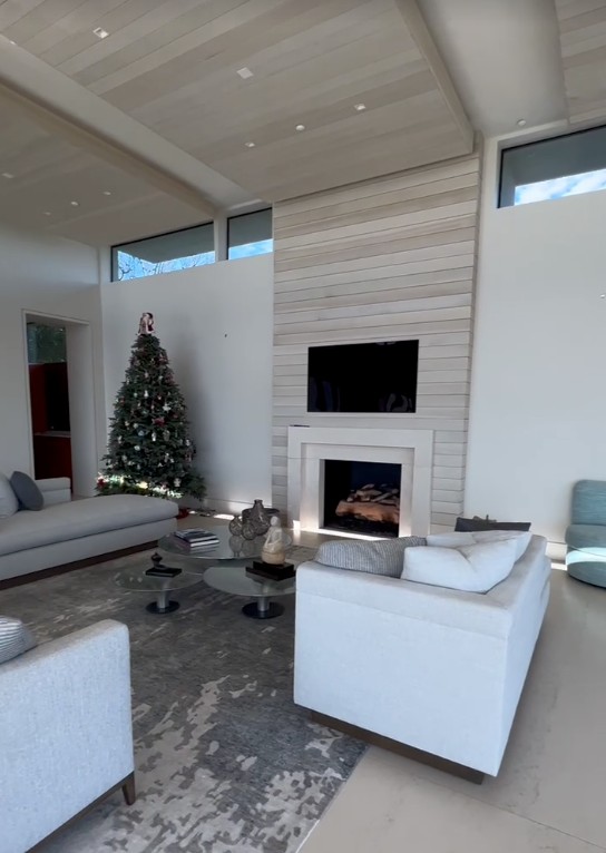 Living room at the Westlake residence with a television above the fireplace, wood-plank ceiling, and light furnishings