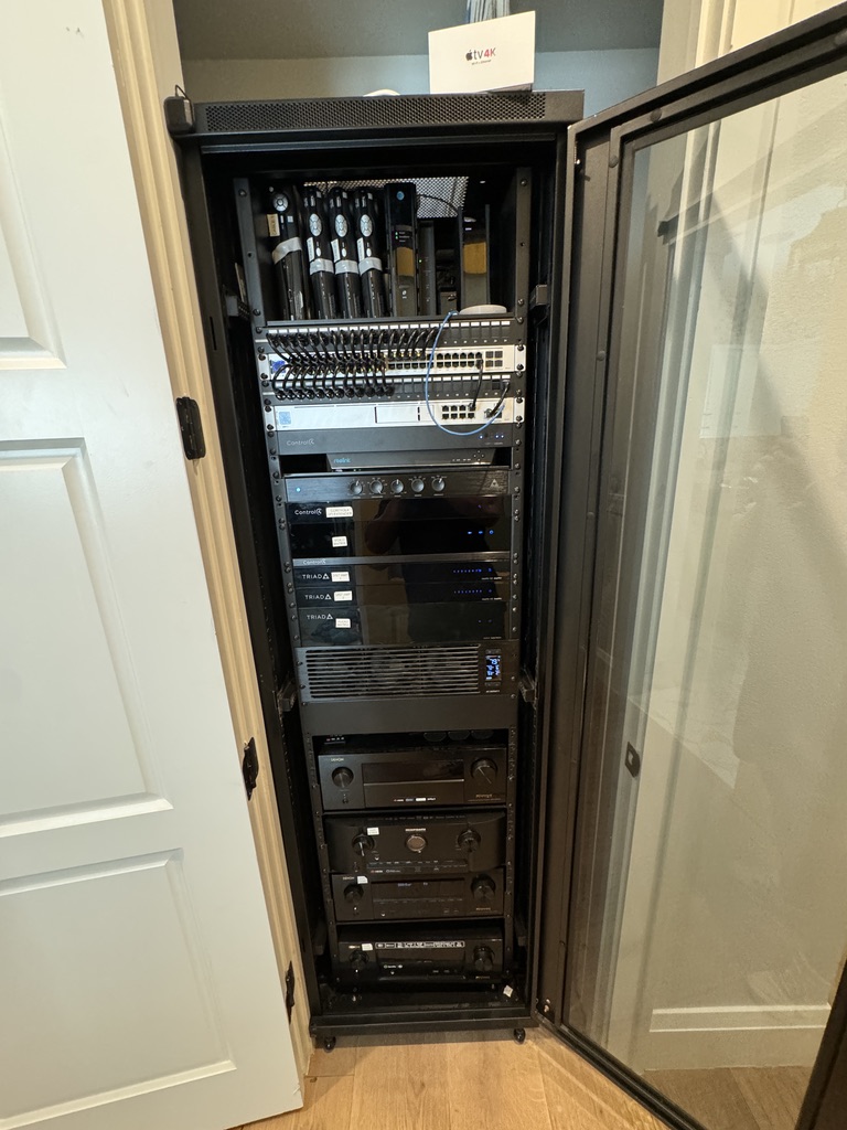Completed network and audio equipment rack behind glass cabinet doors